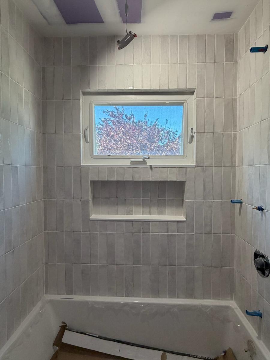 Hall bathroom after renovation: floor-to-ceiling stacked tile, recessed niche, new window and a soaking tub
