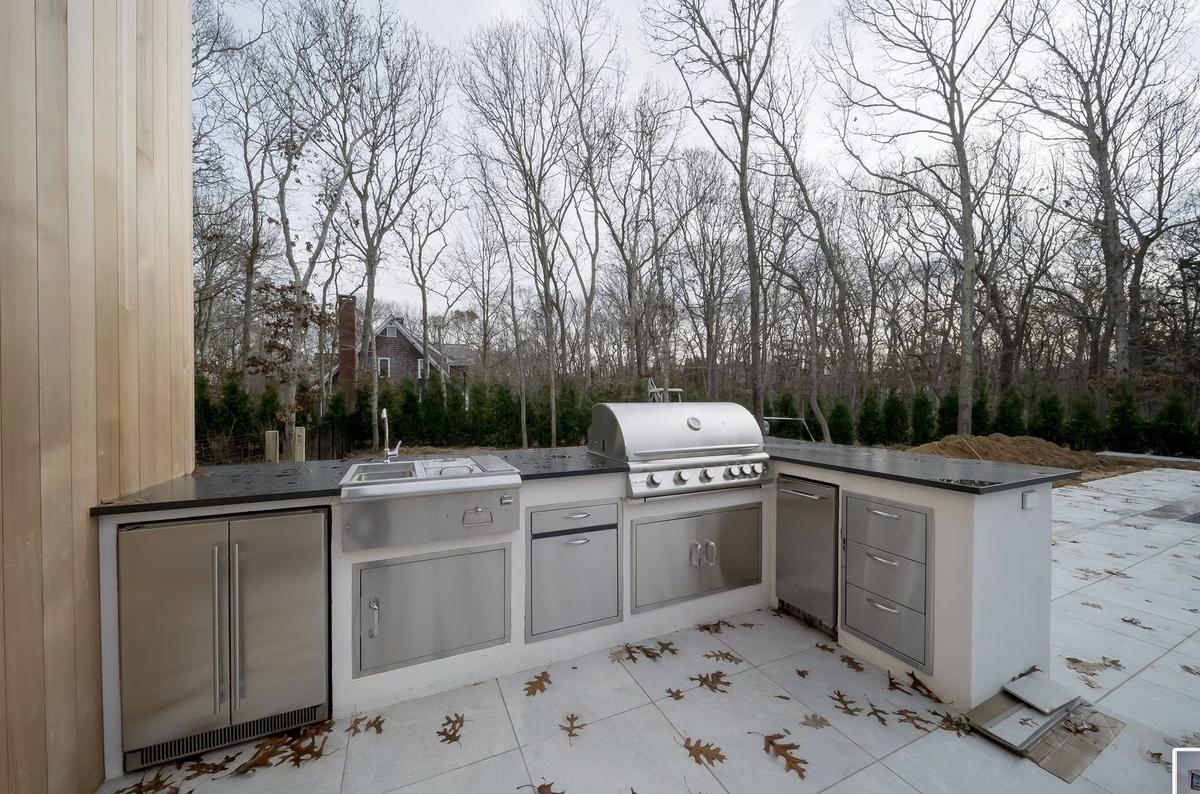 Outdoor kitchen with stone countertops and built-in grill in East Hampton backyard